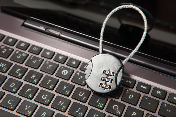 A combination padlock placed on a laptop keyboard with Cyrillic characters, symbolizing data security and anonymization.